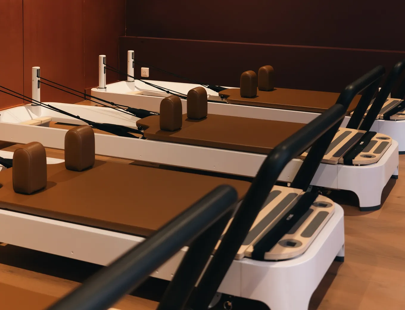 Rangée de Reformers aux chariots de cuir brun alignés dans la salle du studio